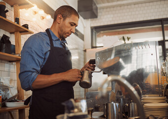 Barista, milk and steam with coffee machine in cafe for espresso, cappuccino and latte with hospitality. African man, jug and froth in restaurant kitchen for warm drink, foam and professional service