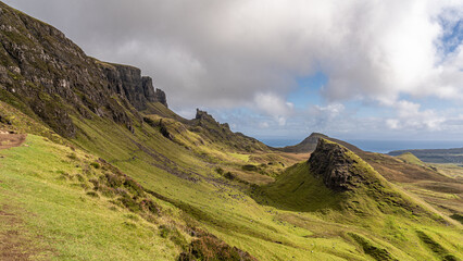 Fototapeta premium Panoramaaufnahme vom The Quiraing bei sonnigem Wetter, im Hintergrund weiße Wolken auf blauem Himmel