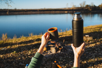 Obraz premium Taking pleasure in a warm and delicious beverage while sitting by the beautiful river a memorable outdoor adventure moment to cherish