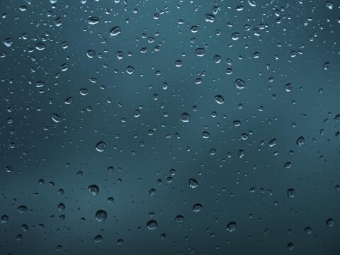 Close-up photo of raindrops on a windowpane, creating a blurred and abstract texture effect, moody aesthetic, cool toned