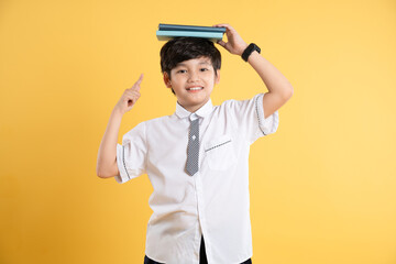 Portrait of Asian kid boy wearing  school uniform and holding book posing on yellow background