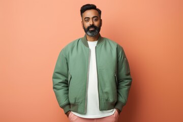 Portrait of a tender indian man in his 40s sporting a stylish varsity jacket in front of solid...