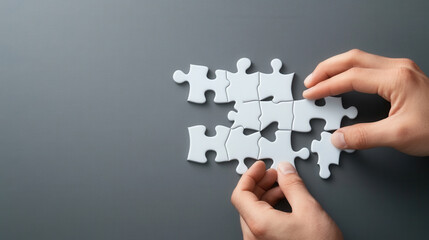 Close up of hands assembling white puzzle on gray background, symbolizing problem solving and creativity