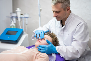 a cosmetologist doctor makes cosmetic procedures on the face of a young guy in a beauty salon