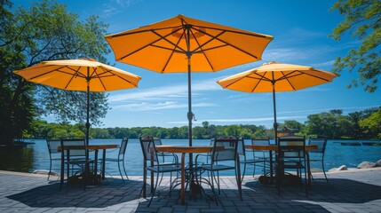 Empty patio tables with yellow umbrellas overlooking a lake on a sunny day.