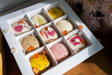 Open gift box with macaron cookies and marshmallow hearts on bed. Gift box with sweets lying on white bed with flowers. Valentine's Day. Gift shopping.