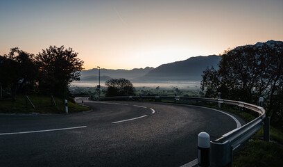 Empty curvy mountain pass at dawn. Mountain valley covered in fog in the background, sky is glowing...