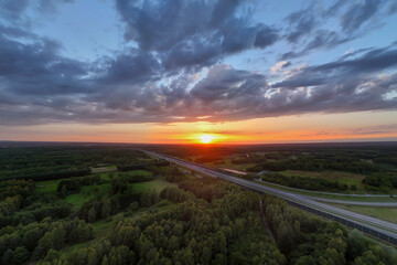 Breathtaking sunset over lush green fields and a highway, casting vibrant colors across the sky. Perfect for nature and travel themes.