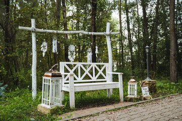 In the heart of a beautiful, serene forest, there is a white wooden bench that is positioned gracefully amidst the surrounding trees and greenery, inviting visitors to rest and enjoy nature