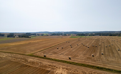 Fototapeta premium Aerial view of a vast agricultural field with rolled hay bales under a clear sky, showcasing the beauty of rural landscapes.