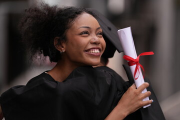 Two graduates in caps and gowns beam with joy, embracing and cheering in celebration. Their wide...