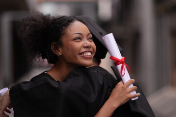 Two graduates in caps and gowns beam with joy, embracing and cheering in celebration. Their wide...