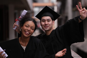 Two graduates in caps and gowns beam with joy, embracing and cheering in celebration. Their wide...