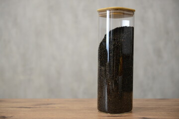 A clear glass container filled with black tea mixture sitting on a wooden table against a light textured background