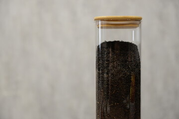 A clear glass container filled with black tea mixture sitting on a wooden table against a light textured background