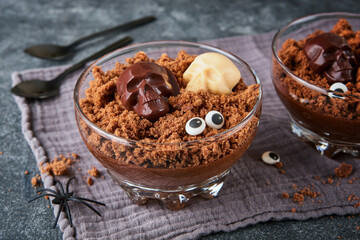 Halloween party chocolate puddings or Panna Cotta with brownie crumbles and chocolate sculls served in clear glass on grey dark background. Party idea for Halloween.