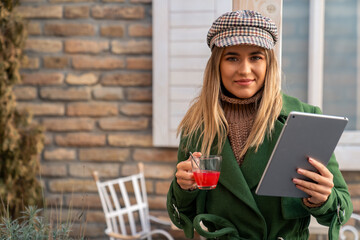 A cheerful Caucasian woman enjoys a cozy autumn day outside, engaging with her digital tablet while...
