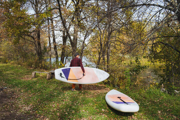 A man, deeply immersed in thought, meticulously carries two surfboards through a vibrant, lush...