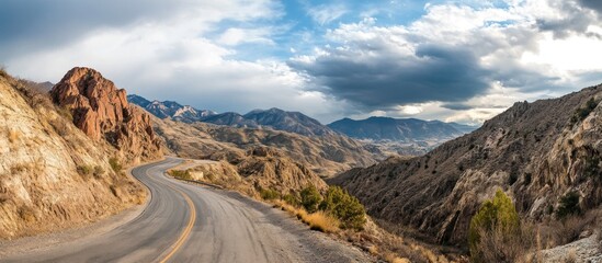 Winding road through mountains with dramatic clouds overhead.
