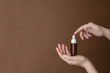 Hand holding serum glass bottle or essential oil on brown background. Natural Organic Spa Cosmetic concept