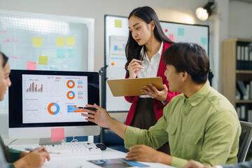 Business team discussing marketing strategy analyzing charts on computer screen and clipboard, working together in modern office