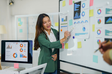 Businesswoman pointing at charts and statistics on whiteboard during a presentation in a modern...