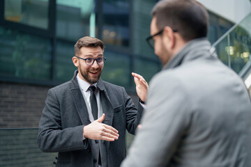Two mid-adult Caucasian businessmen engage in a discussion, one gesticulating as they collaborate...
