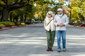 Obraz premium Elderly beautiful married couple on a walk in an autumn park