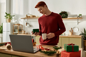 With a warm smile, a young man holds a gift while sipping a drink in a festive kitchen.