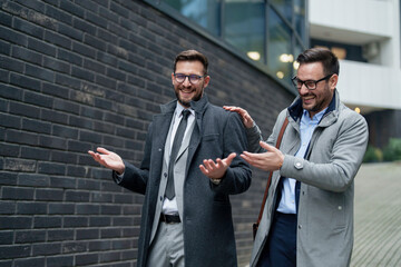 Two cheerful Caucasian mid-adult businessmen relax outside, engaging in a friendly conversation....