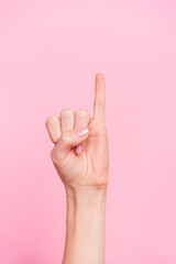 Fototapeta premium Vertical cropped view of attractive girl hand showing small little finger up isolated over pink pastel color background