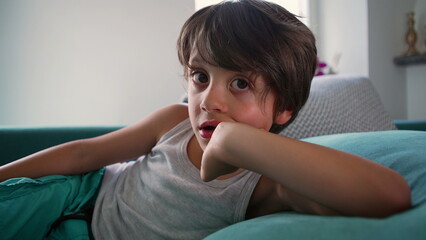 Young boy lying on couch with a thoughtful expression, resting his head on his hand, capturing a...