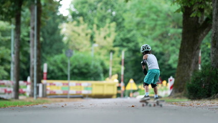 Young boy skateboarding down a pathway, making a swift turn while keeping his arms outstretched for...