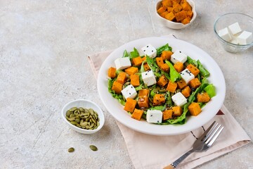 Healthy salad of romaine lettuce, baked pumpkin, feta cheese and mixed seeds in a light ceramic plate on a light concrete background. Recipes pumpkin.