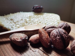 Honey in honeycomb with wooden spoon, almonds and walnuts in shell