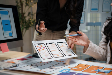 Web designers working together analyzing mobile app software development prototype on paper