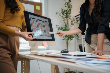 Two ux designers collaborating on a wireframe for a mobile application, using sticky notes and a desktop computer in their office