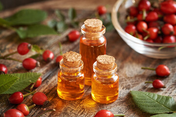 Three bottles of rose hip seed oil with fresh rosehips