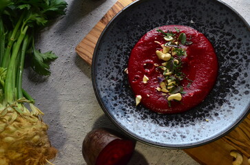 color photo of food, vegetarian food, beetroot and chickpea hummus, cashew nuts, celery, dark rustic plate, close-up view