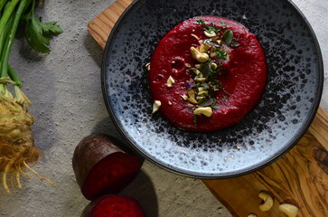 A vibrant and creamy beetroot chickpea hummus, elegantly served on a rustic speckled plate and topped with crunchy cashew nuts and fresh herbs