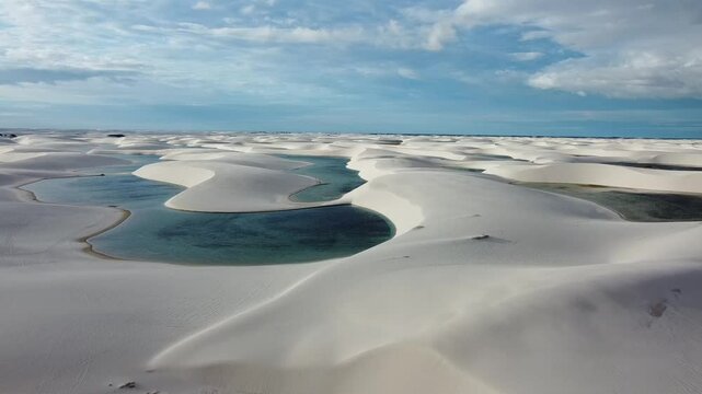 A drone reveals the vast white dunes of Len&ccedil;&oacute;is Maranhenses, with shimmering lagoons nestled between the rolling sands. The sweeping aerial view captures the stunning contrast of the endless desert.