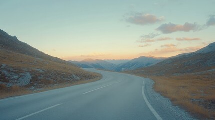 Fototapeta premium A winding road through mountainous terrain during dawn in a serene valley surrounded by peaks