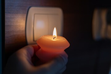 Burning candle in hand near light switch in darkness. Power outage due to war in Ukraine	