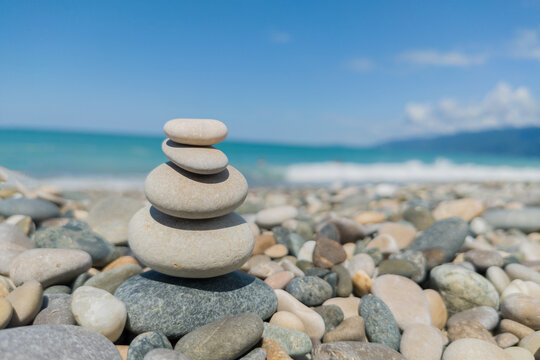 Pebble grey stones on top of each as pyramid or heap on seashore with acean water.Metaphor of calmness, harmony and tranquility, stress