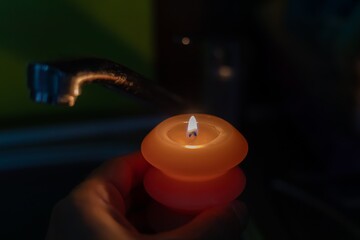 Burning candle in hands near faucet in kitchen in darkness. Power outage due to war in Ukraine