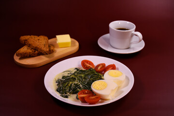 Healthy breakfast. Fresh boiled eggs with cherry tomatoes and spinach in cheese sauce. Coffee and buttered toast. Proper nutrition.