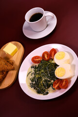 Healthy breakfast. Fresh boiled eggs with cherry tomatoes and spinach in cheese sauce. Coffee and buttered toast. Proper nutrition.