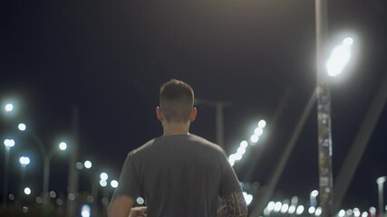 Unrecognizable man running through an illuminated city street at night. Tracking shot capturing movement and urban energy under bright streetlights.