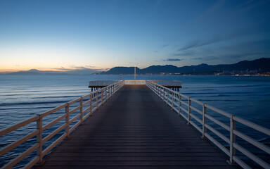 A wooden pier stretches towards the horizon  with blue water and a distant city skyline  evoking a sense of tranquility and escape   