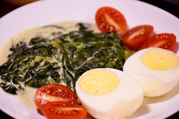 Healthy breakfast. Fresh boiled eggs with cherry tomatoes and spinach in cheese sauce. Coffee and buttered toast. Proper nutrition.